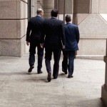 Three businessmen walk along a promenade on Wall Street in the financial district of New York